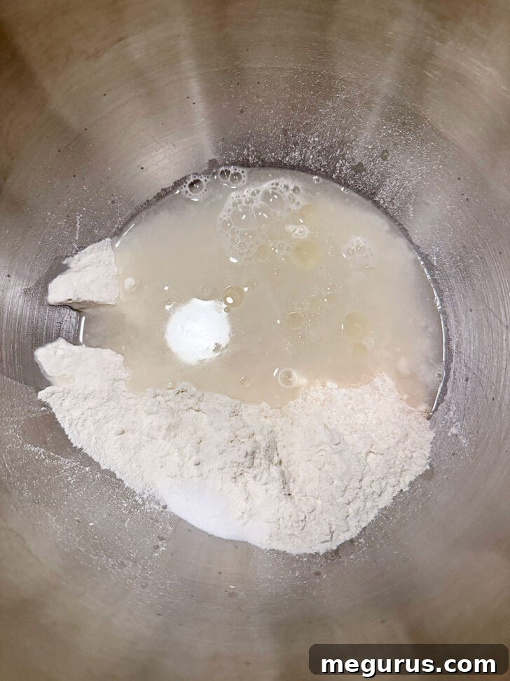Focaccia dough ingredients in the bowl of a stand mixer, ready for mixing.