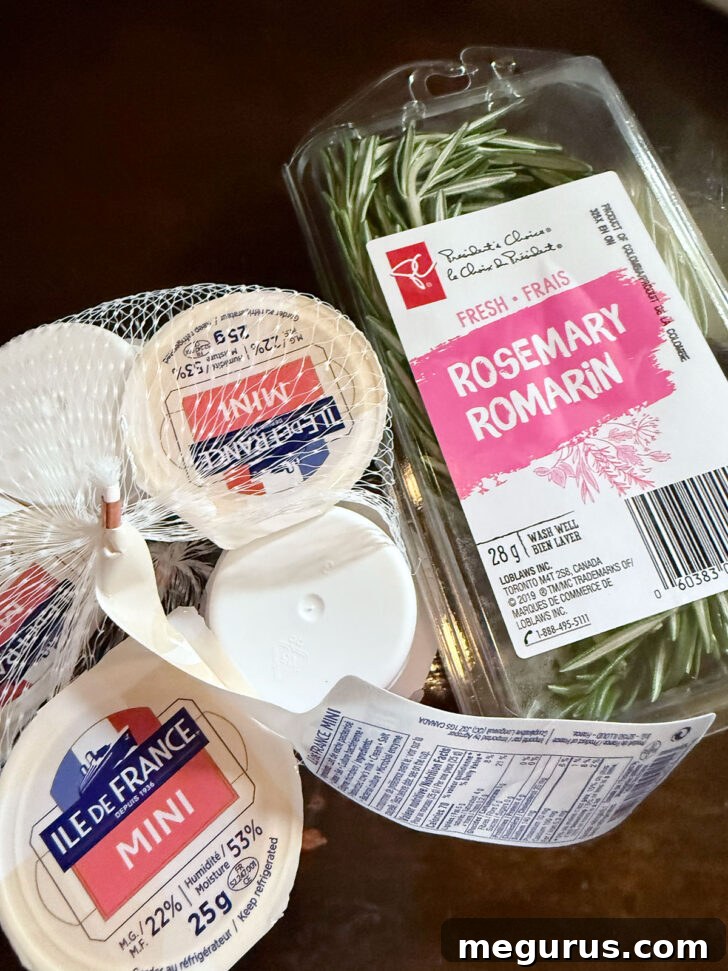 Packages of mini Brie cheese rounds and fresh rosemary sprigs on a counter.