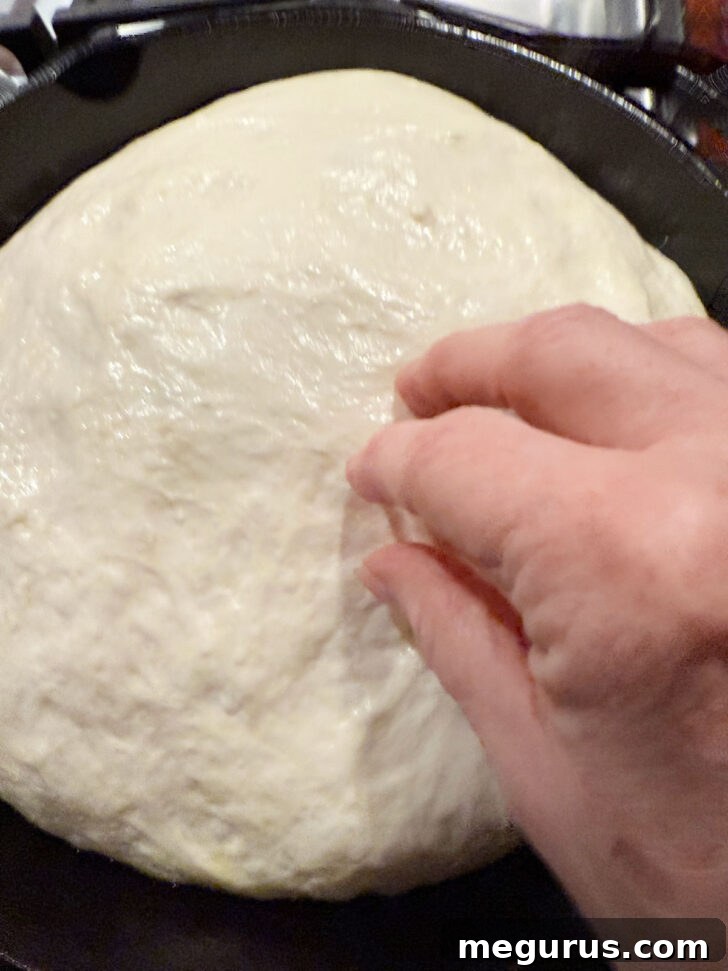 Hands oiling fingertips and poking risen focaccia dough to create dimples.