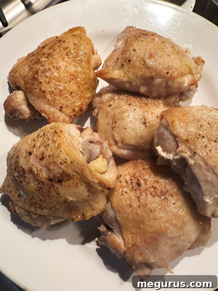 Cooked chicken thighs gently lifted from the skillet onto a waiting plate.