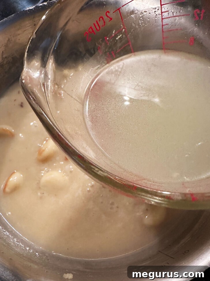Adding chicken broth to the skillet with garlic and wine, whisking to combine.