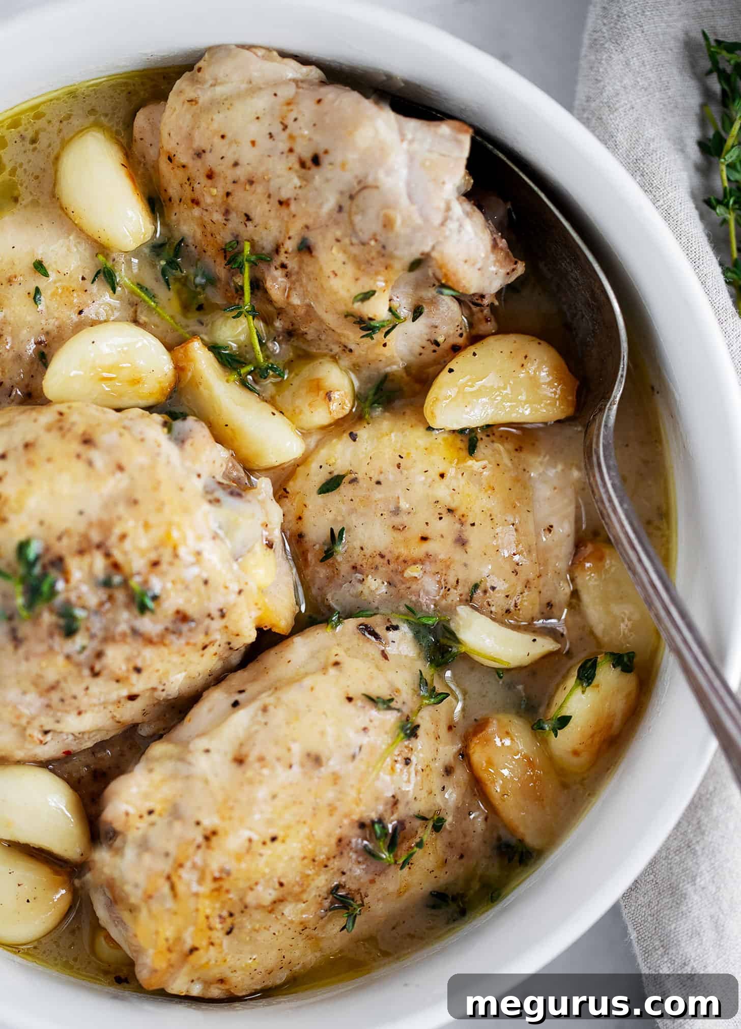 A close-up of rustic garlic chicken with a generous amount of gravy in a bowl, accompanied by a spoon, highlighting its comforting appeal.
