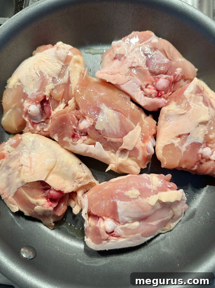 Chicken thighs being carefully placed skin-side down into a hot skillet with oil.