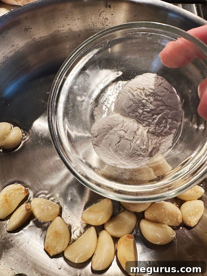 Flour being sprinkled over the golden garlic cloves in the skillet.