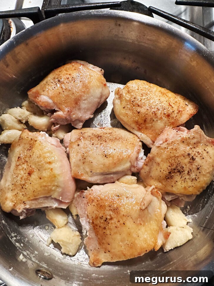 The browned chicken thighs returned to the skillet with the garlic and flour mixture.