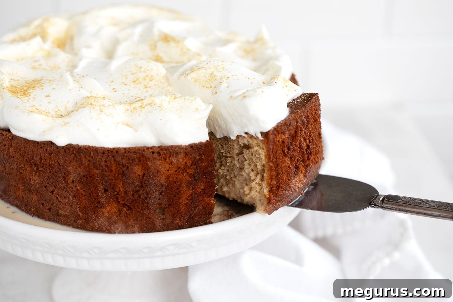 Gingerbread tres leches cake sliced on cake plate, showcasing its moist texture and creamy topping.