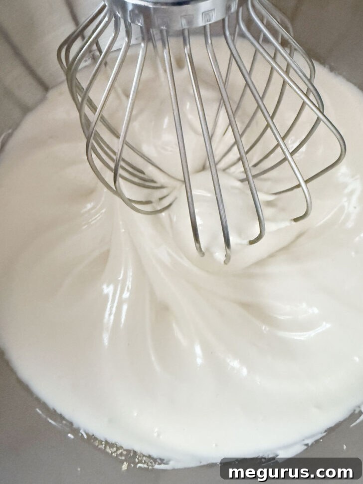 Finished whipped egg whites in mixer, forming soft, glossy peaks.
