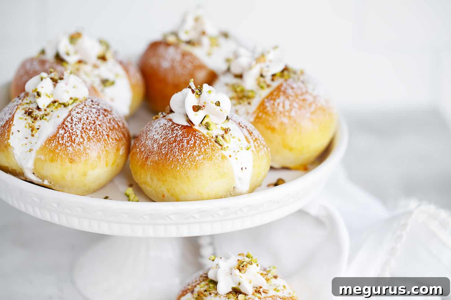 Pistachio maritozzi on a cake plate, showcasing their whipped cream filling and chopped pistachio garnish.