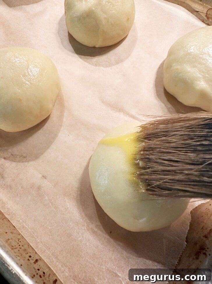 Brushing the maritozzi with egg wash before baking to achieve a golden crust.