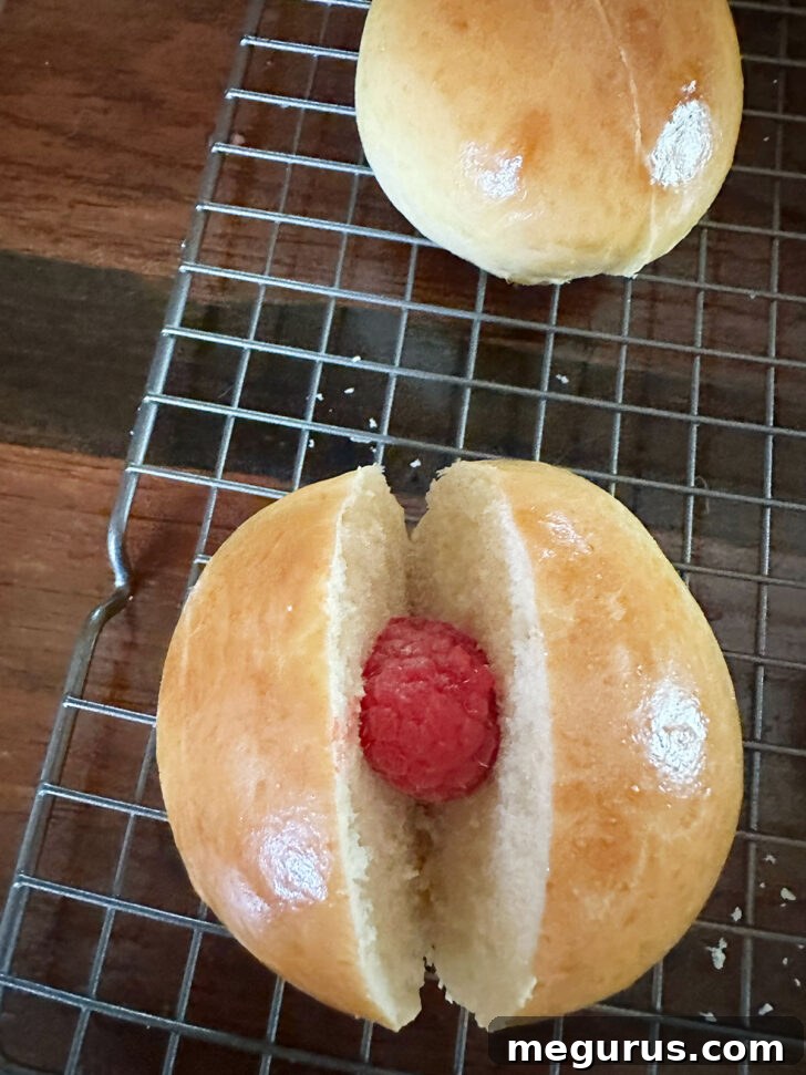 Placing a fresh raspberry into the maritozzi before filling with cream.