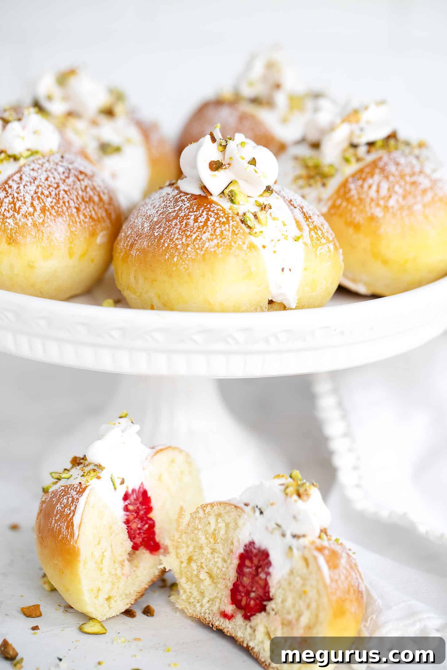 Maritozzi on serving stand with one cut open, showing the cream and raspberry filling.