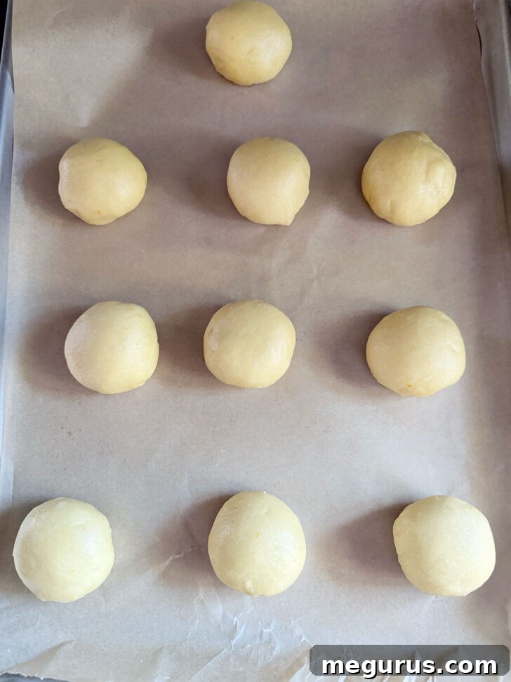 Formed buns arranged on a parchment-lined baking sheet for their second rise.
