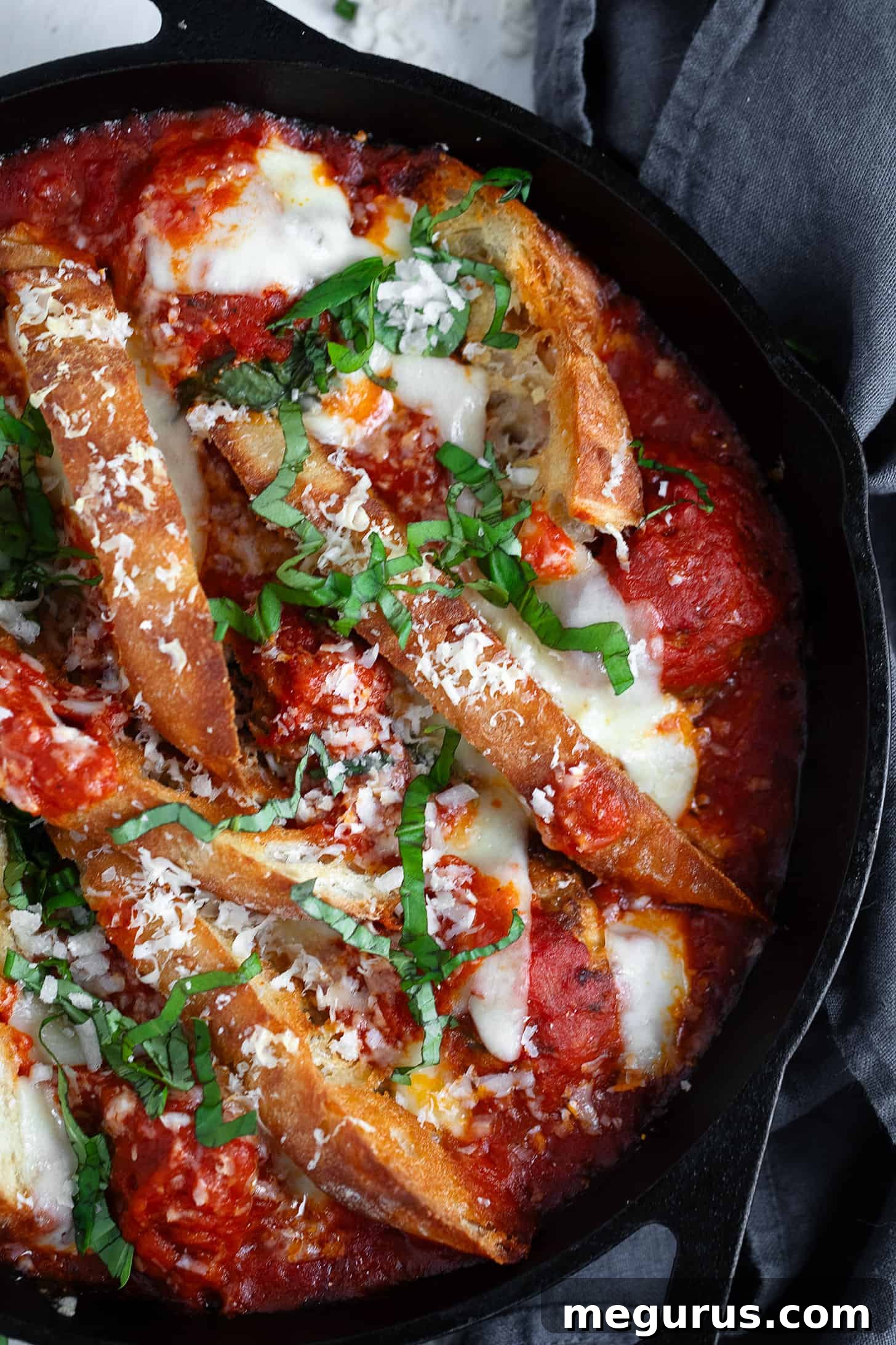 Close-up of the finished meatball sub casserole in a skillet, garnished with fresh basil.