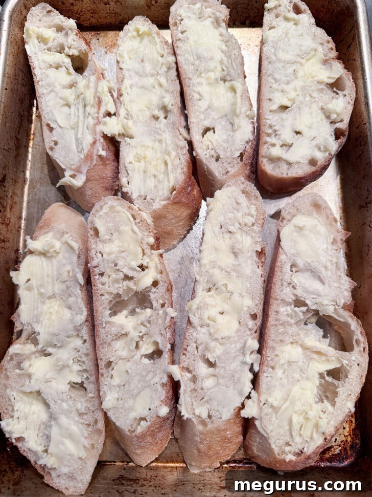 Baguette slices coated with garlic butter on a baking sheet, ready for the oven.