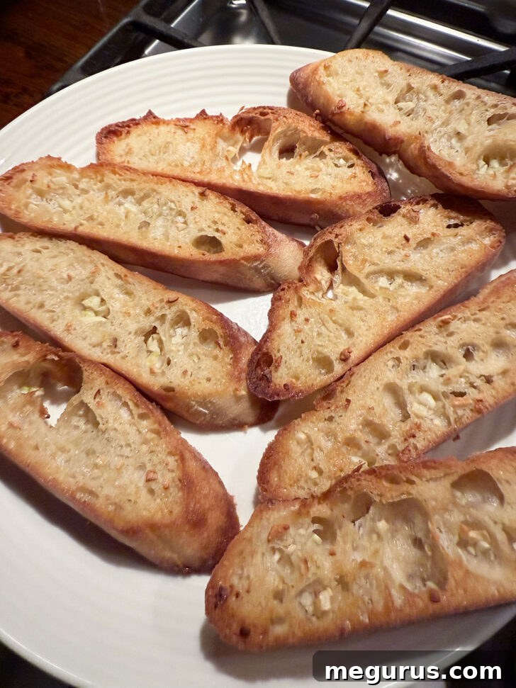 Crispy golden garlic bread slices cooling on a plate after baking.