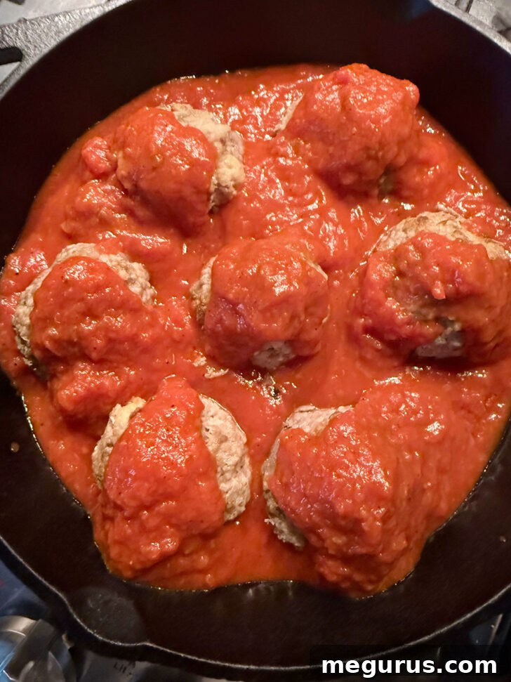Additional marinara sauce drizzled over the meatballs in the skillet.