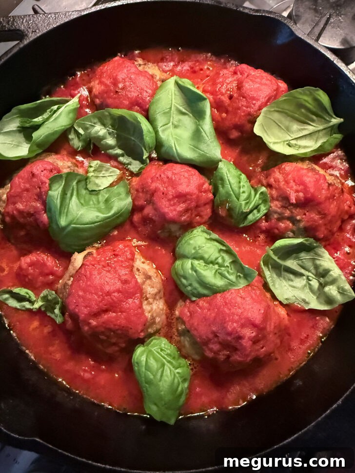 Fresh basil leaves scattered over the meatballs and sauce in the skillet.