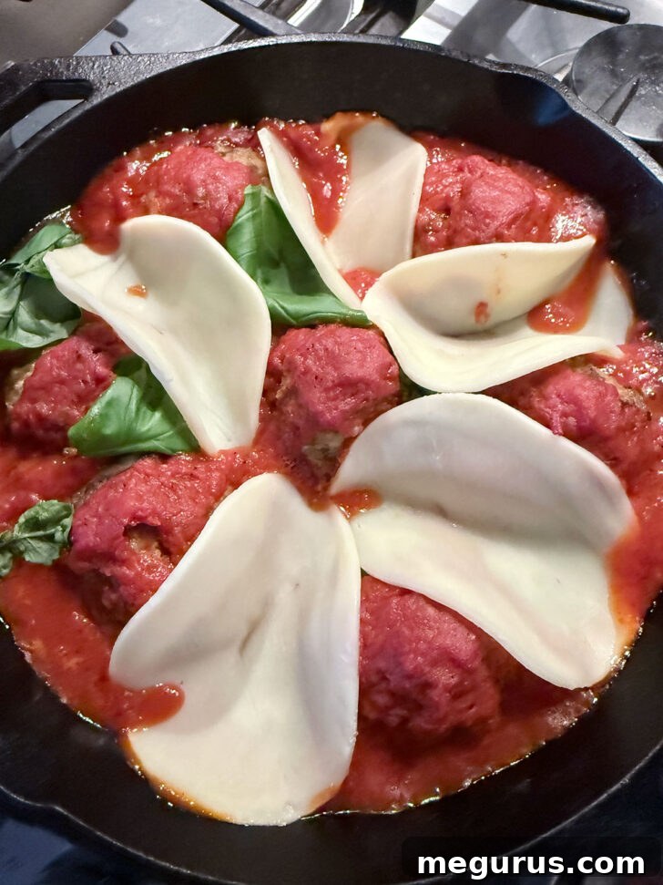 Slices of provolone cheese tucked alongside the meatballs in the skillet.