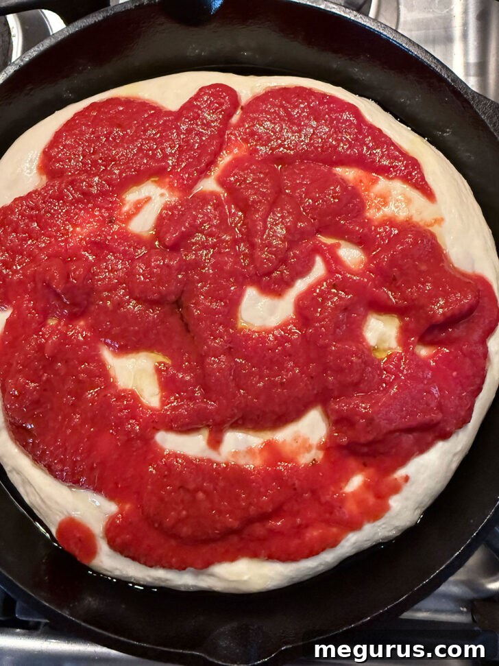 Pizza sauce being spooned evenly over the risen focaccia dough.
