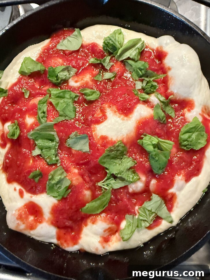 Torn fresh basil leaves scattered over the pizza sauce on the focaccia dough.