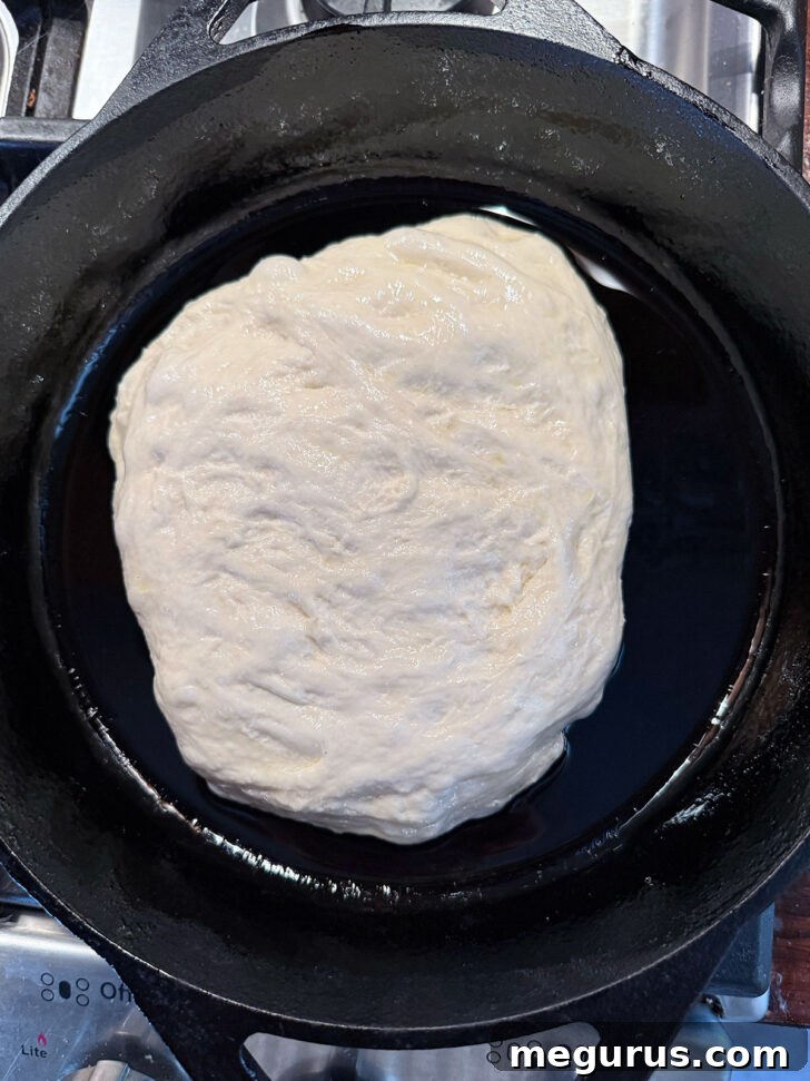 Sticky focaccia dough carefully added to the greased cast iron skillet.