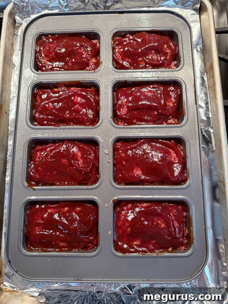 Mini meatloaves neatly arranged in a loaf pan, topped with homemade BBQ sauce, ready for baking.