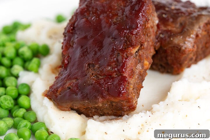 Meatloaf with homemade bbq sauce on plate with mashed potatoes and peas.