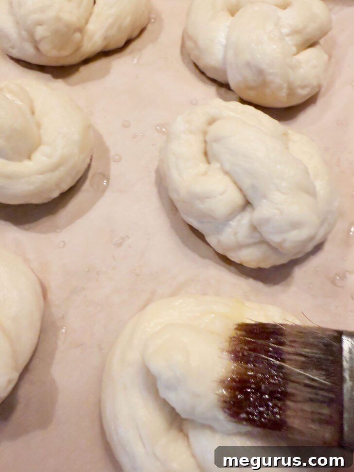 Brushing the boiled pretzels with melted butter on a baking sheet.