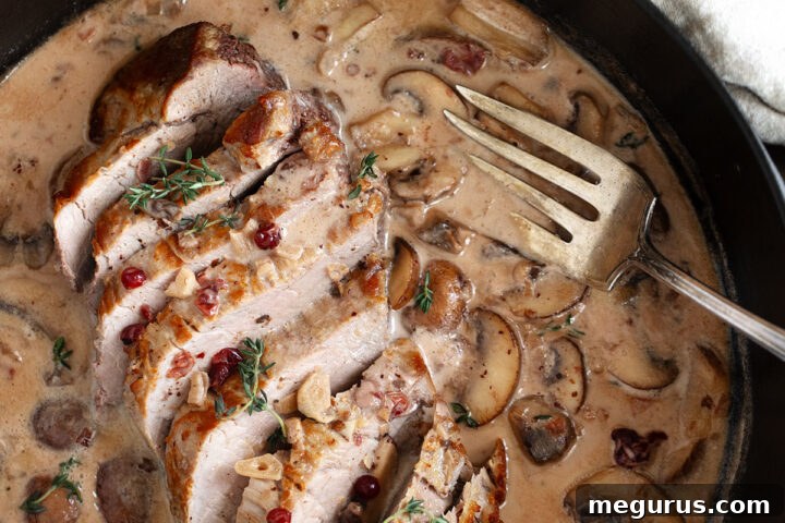Pork tenderloin with a creamy mushroom and lingonberry jam sauce in skillet.