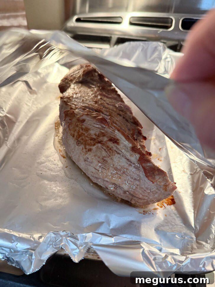 Pork tenderloin after cooking resting under a foil tent.