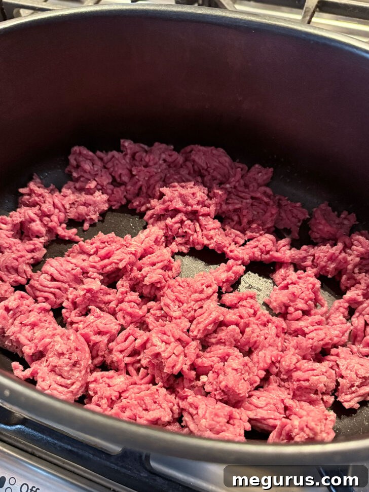 Ground beef added to a skillet on the stovetop, beginning to brown.