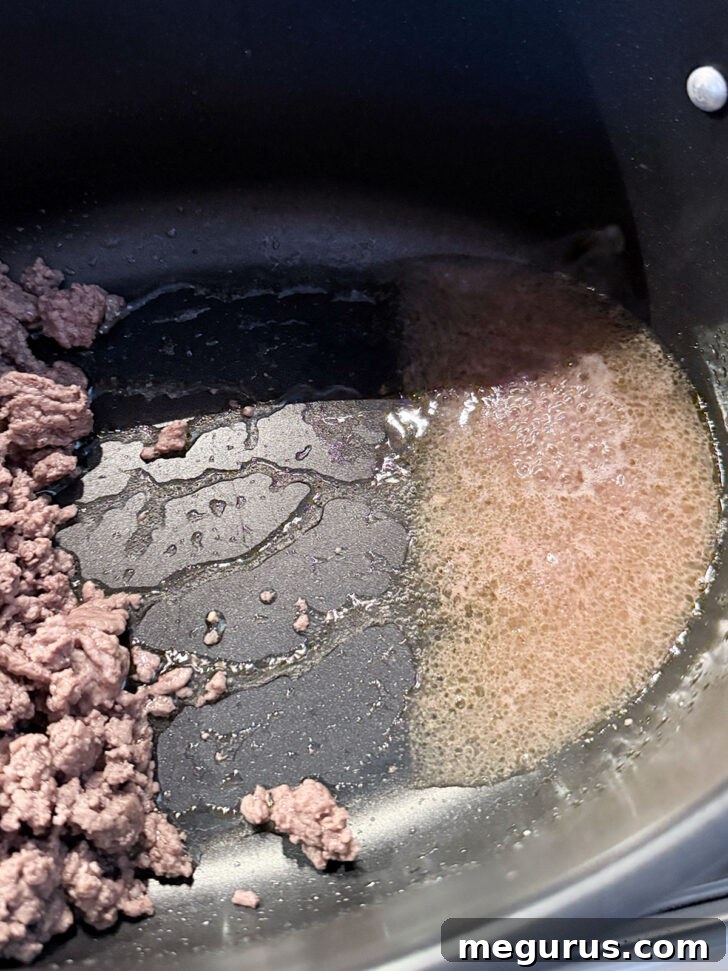 Excess fat being spooned off from the ground beef in the skillet.