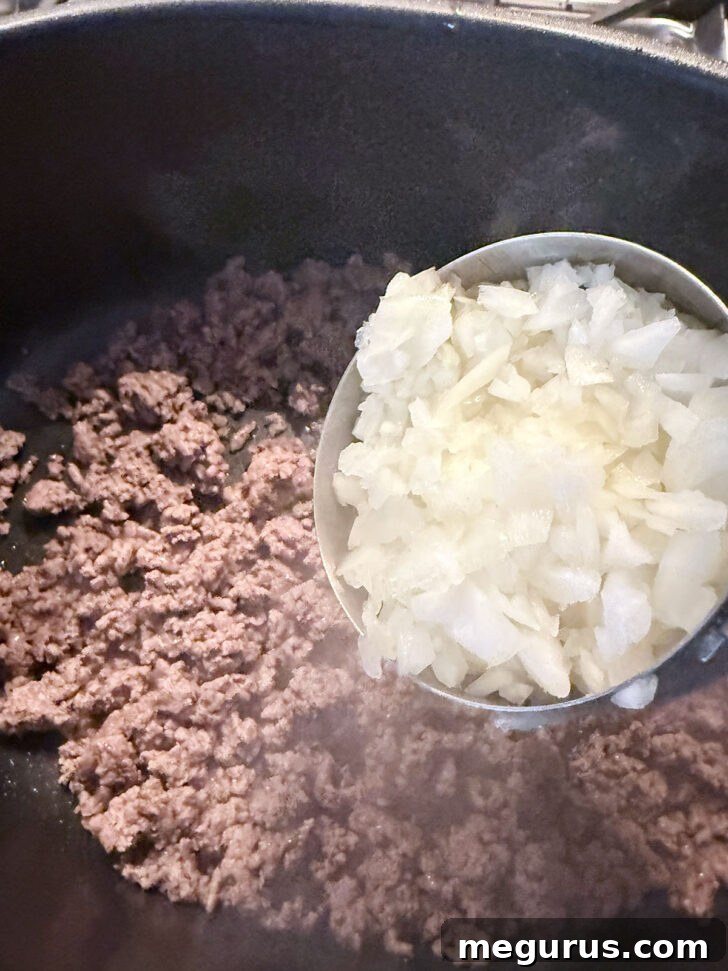 Diced onions being added to the skillet with browned ground beef.