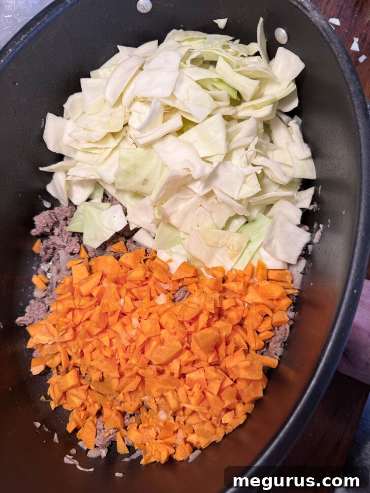 Browned ground beef, chopped cabbage, and carrots added to the slow cooker.