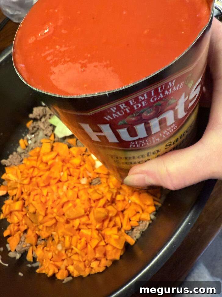 Canned tomato sauce being poured into the slow cooker.