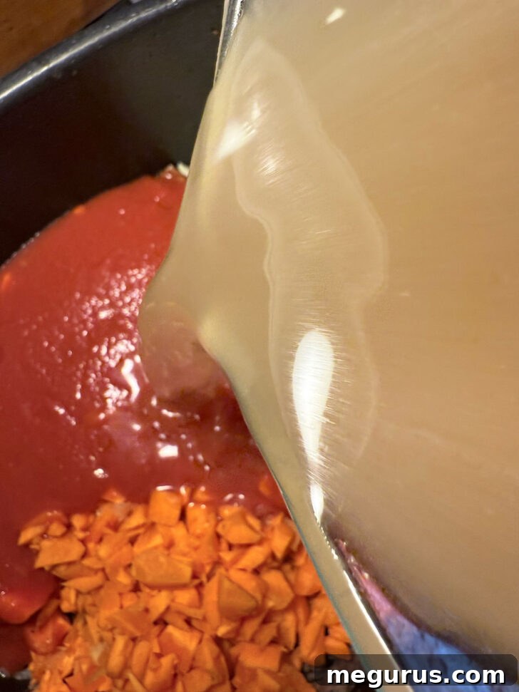 Beef broth being added to the slow cooker with other soup ingredients.