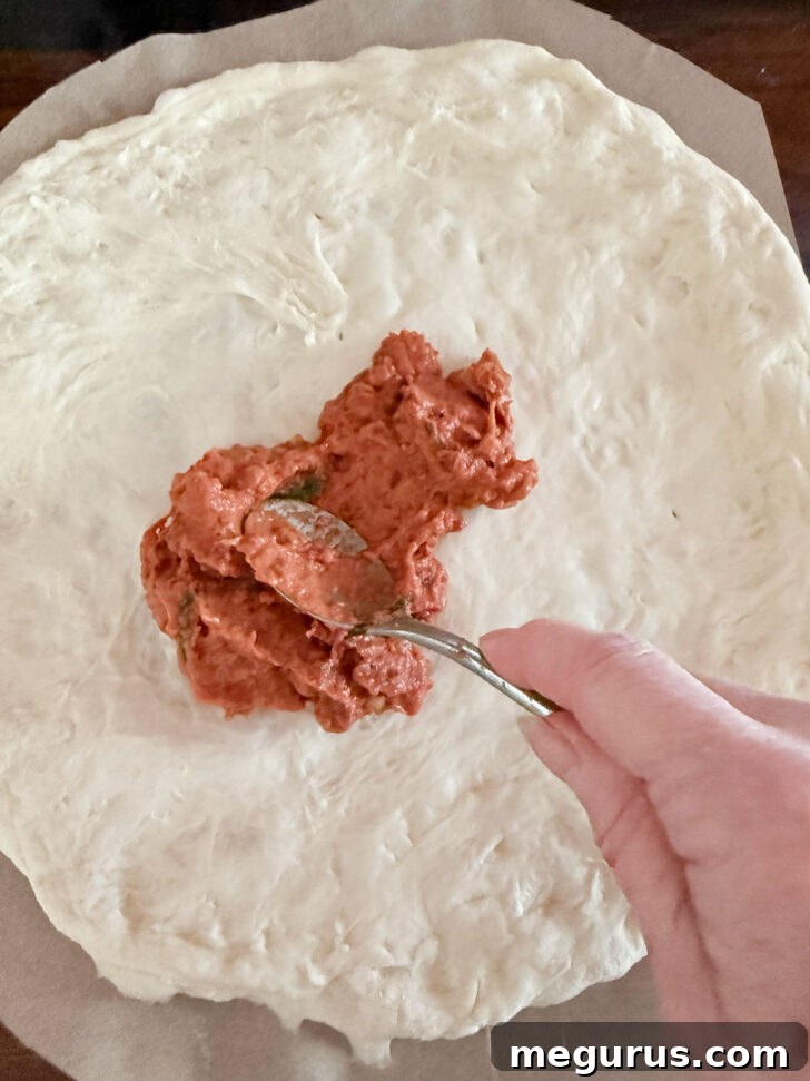 Spreading the vodka sauce onto the pizza dough.