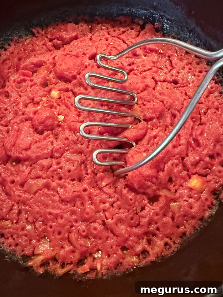 Breaking up the tomatoes in the skillet with a potato masher.