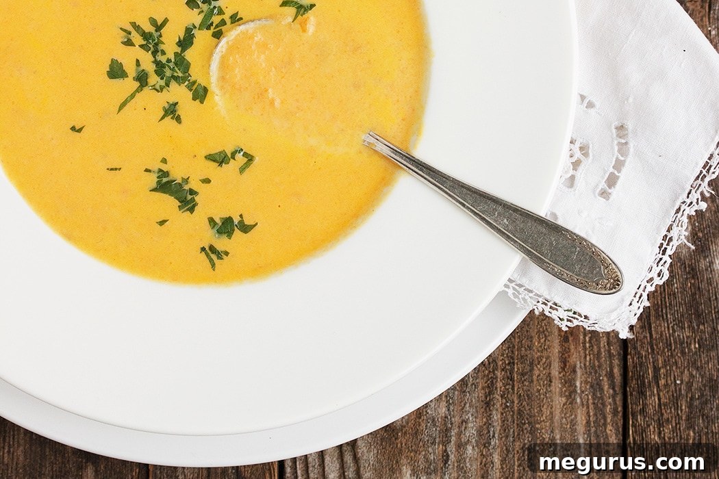 Creamy Carrot Ginger Soup in a white bowl, garnished with fresh herbs.