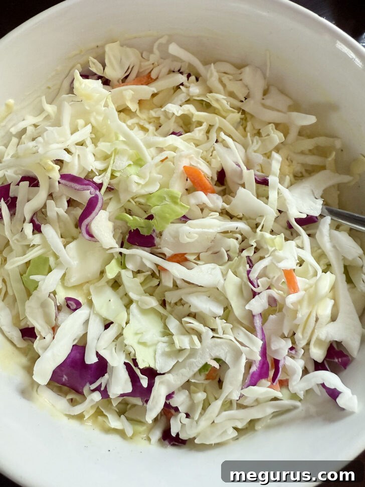 Coleslaw cabbage mix added to the mixed dressing in a large bowl.