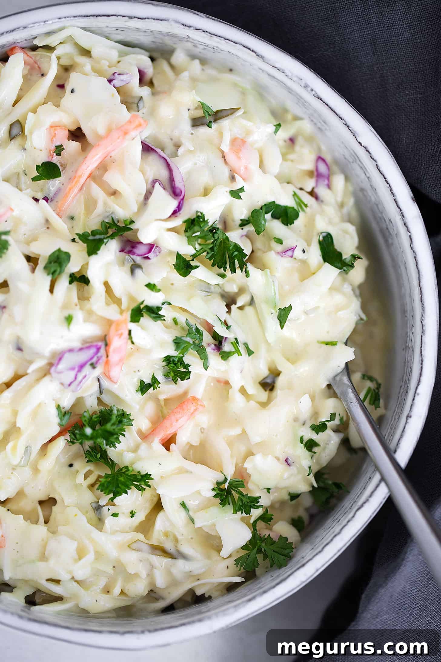 Dill pickle coleslaw in a decorative serving dish with a spoon, ready to be served at a gathering.