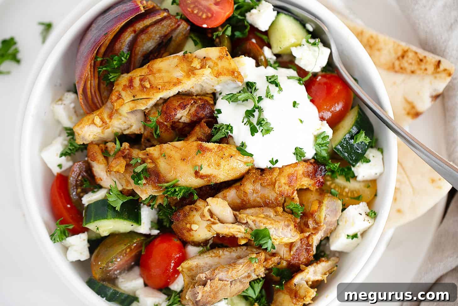 Chicken shawarma bowl with rice, tomatoes, cucumber and white sauce, garnished with fresh parsley.