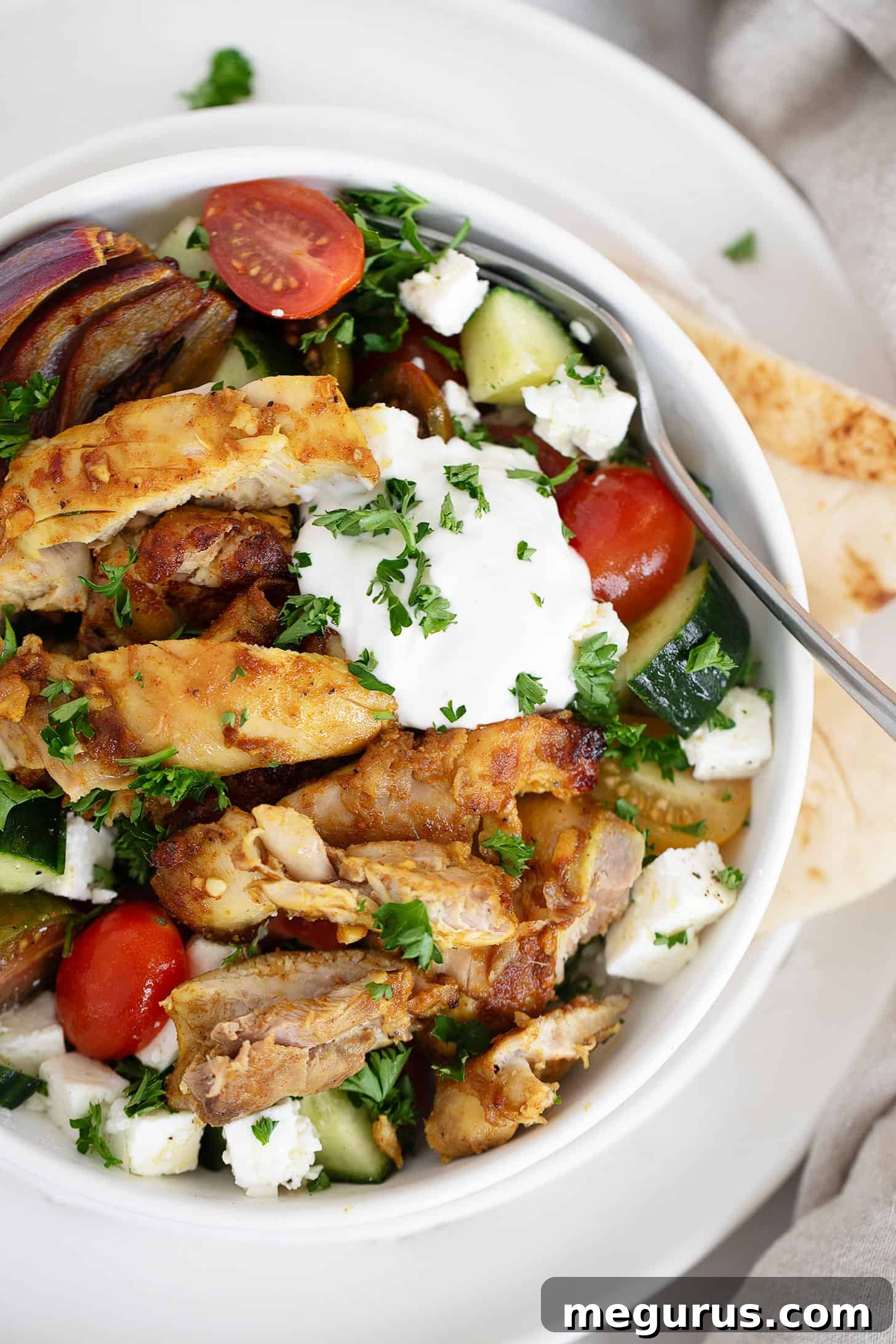 Close-up of a finished Chicken Shawarma Bowl, showcasing the chicken, vegetables, and creamy white sauce.