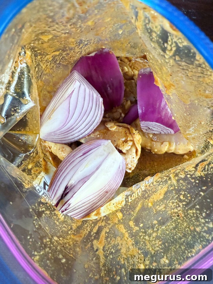 Red onion added to zipper bag with the chicken and marinade, ready for baking.