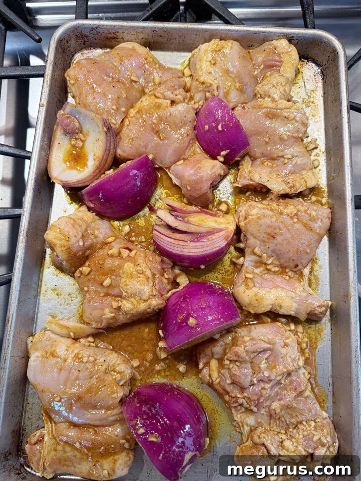 Onion and marinated chicken spread out on a baking sheet before cooking.