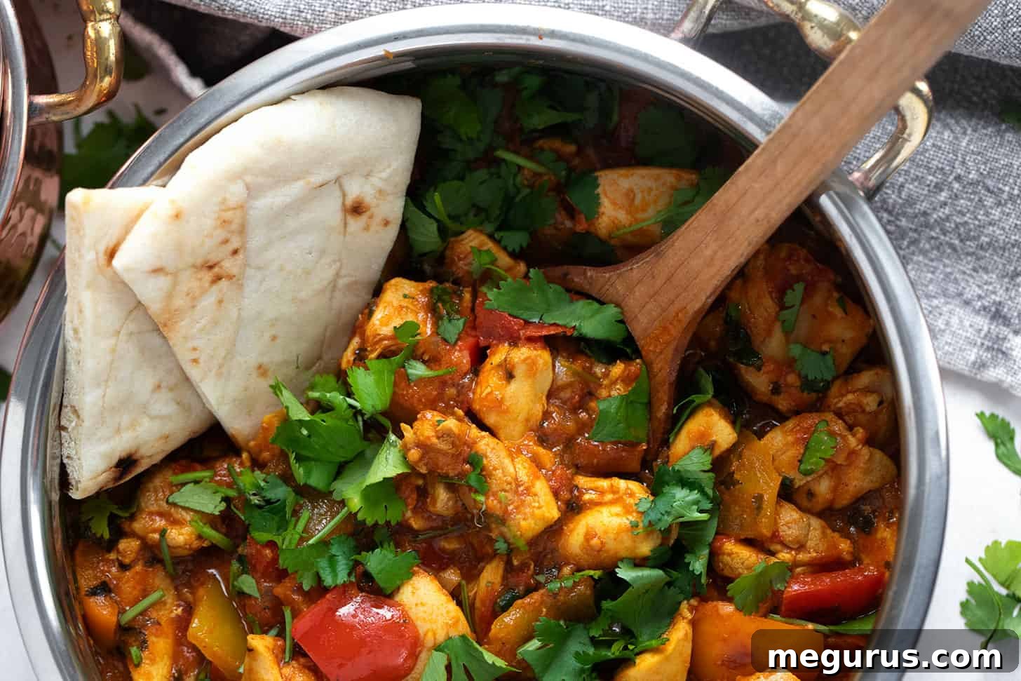 A glistening copper serving bowl filled with authentic Chicken Jalfrezi, garnished with fresh cilantro, alongside warm naan bread, ready to be enjoyed.