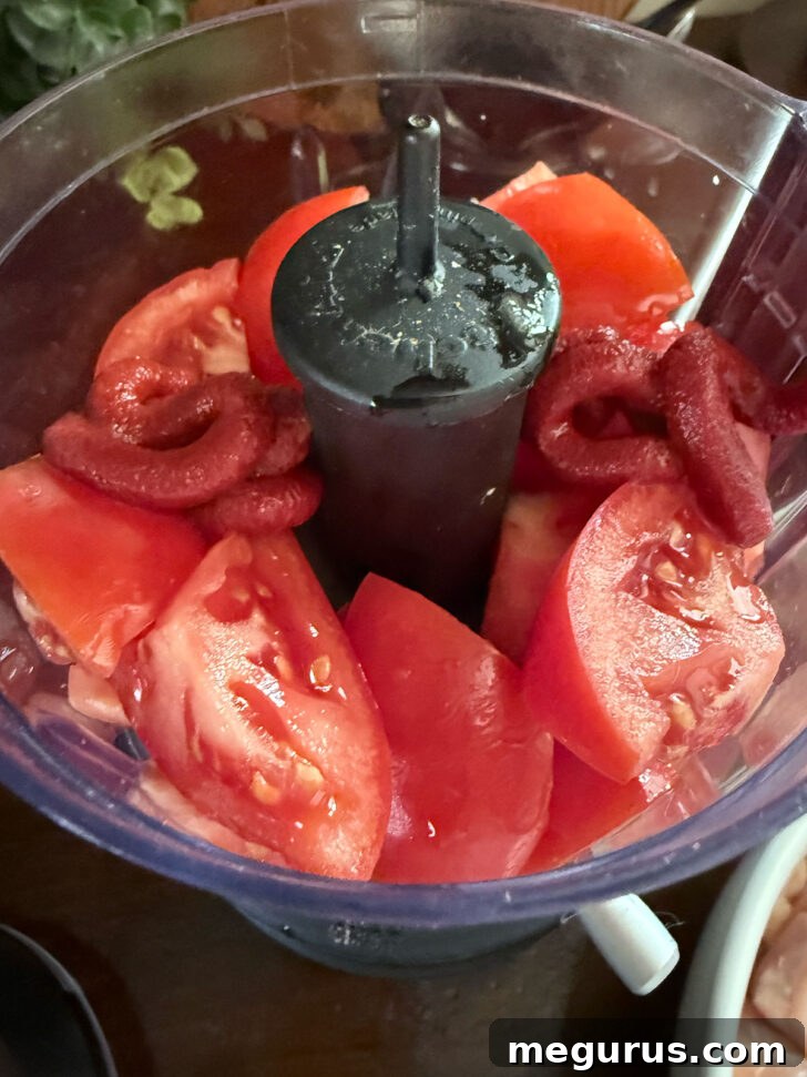 Fresh tomatoes and rich tomato paste ready to be pureed in a food processor, forming the base of the jalfrezi sauce.