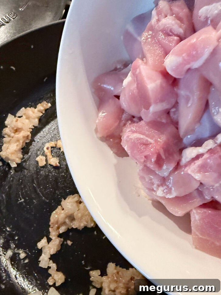Cubed boneless chicken thighs added to a skillet with sautéed onions and ginger-garlic paste, cooking until lightly browned.