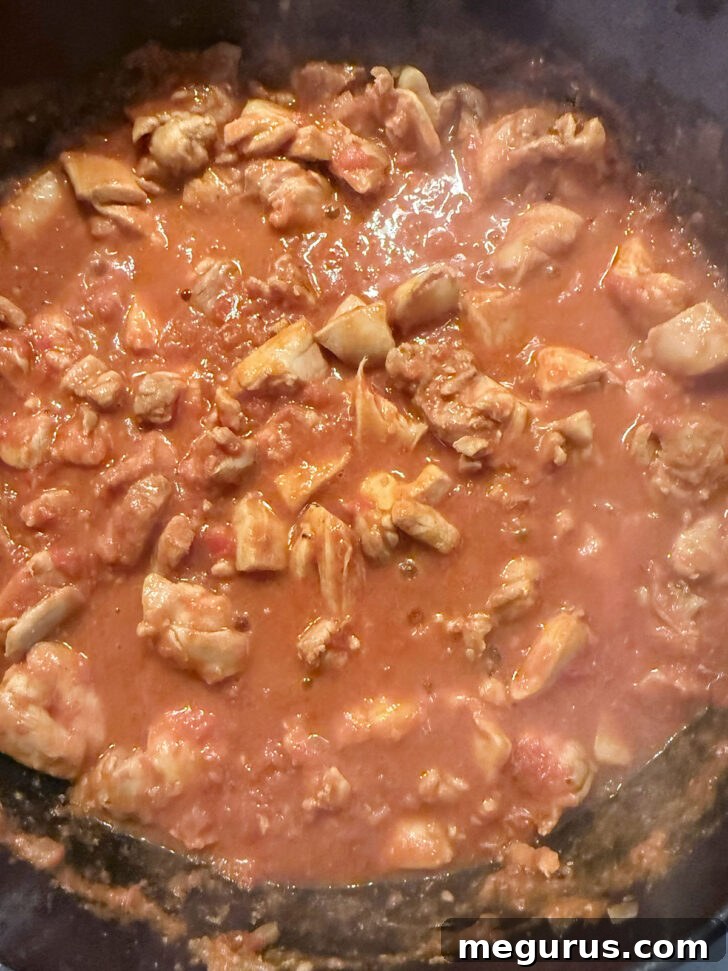 Chicken Jalfrezi gently simmering in a skillet, partially covered, allowing the rich flavors to meld and the chicken to cook through.
