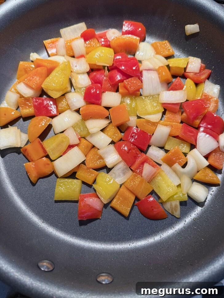 Vibrant bell peppers and chopped onions sizzling in a separate skillet, being stir-fried until softened and slightly caramelized.